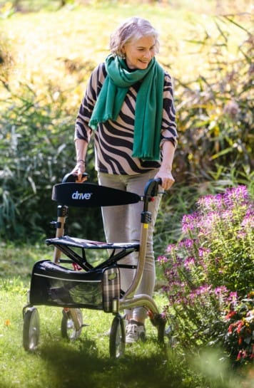 Drive Rollator Nitro met zachte banden in champagne, gebruikt buiten op tuinpad voor stabiel en comfortabel lopen