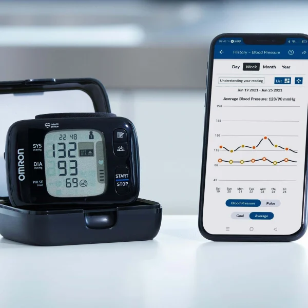 Omron RS7 Intelli IT pols bloeddrukmeter in houder naast smartphone met OMRON connect-app en bloeddrukgrafieken.