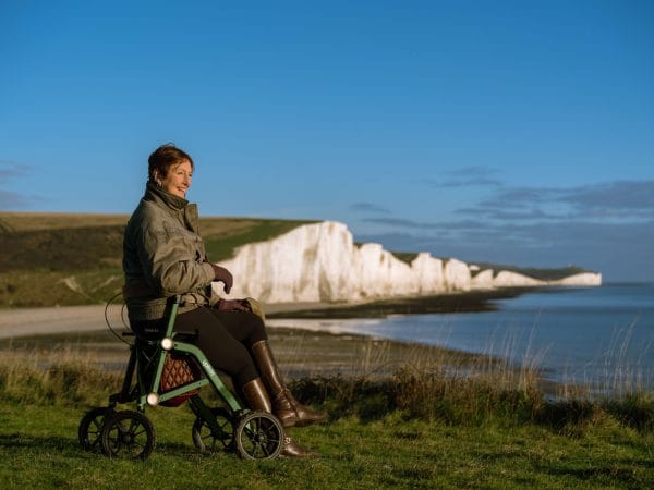 Vrouw zit op de Trive All Terrain rollator van Uplivin en geniet van het uitzicht. De combinatie van lichtgewicht ontwerp, luxe zitvlak en verstelbare handgrepen zorgt voor comfort en elegantie.
