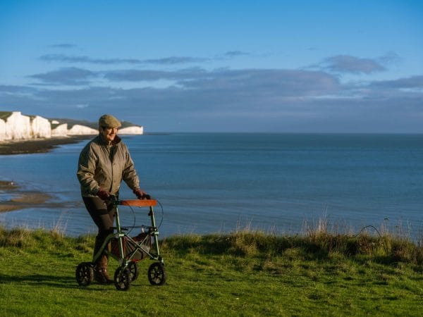 Dame wandelt buiten met de Uplivin Trive All Terrain rollator en geniet van comfort en stabiliteit. De rollator beweegt moeiteloos over verschillende ondergronden en ondersteunt een actieve levensstijl.