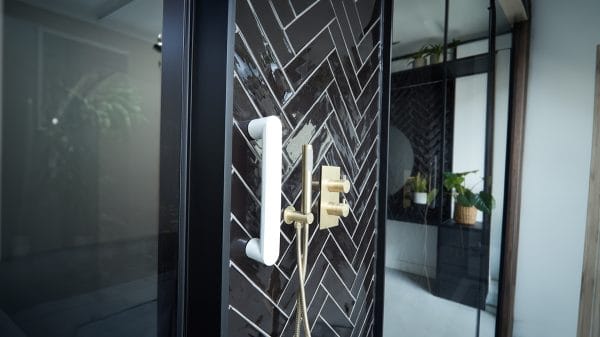 Close-up rechterzijde van Vitility ID Wandbeugel (35/55 cm) in Pearl White naast messing douchebediening op donker visgraat.