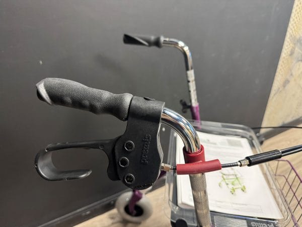 Rollator Premis Provo, zijaanzicht schuin van boven: ergonomische handgreep en rechter eenzijdige rem met rode sleeve.