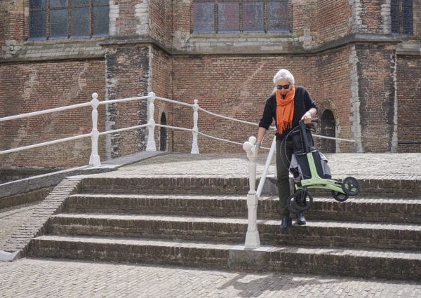Rollz Air carbon rollator, groen: vrouw daalt buiten stenen trap af met zitje en grote wielen; focus op stabiliteit.