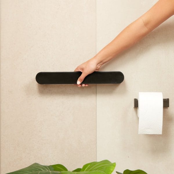 Wandbeugel - Vitility in 35 of 55 cm, zwart; schuin aanzicht met hand, naast toiletrolhouder op beige muur.