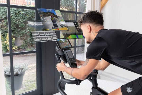 Man traint thuis op de VirtuFit ETAPPE 2.0i indoor cycle bike met tablet en interactieve trainingsapps voor virtuele routes en weerstandsregeling.