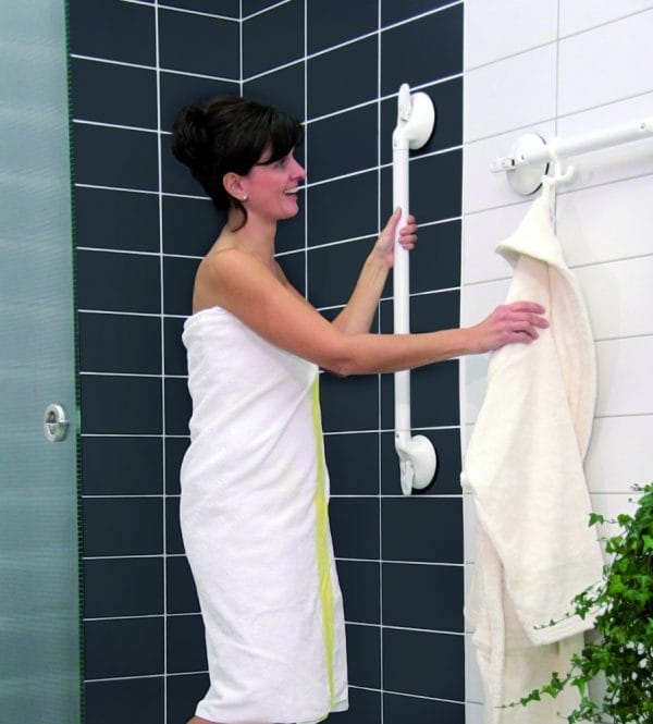 Mobeli wandbeugel met zuignap in badkamer, vrouw ondersteunt zich aan witte wandbeugel naast douche en handdoekrek.