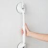 Mobeli verstelbare witte wandbeugel met zuignappen aan tegelwand, vastgepakt door een hand voor extra steun in badkamer of toilet.