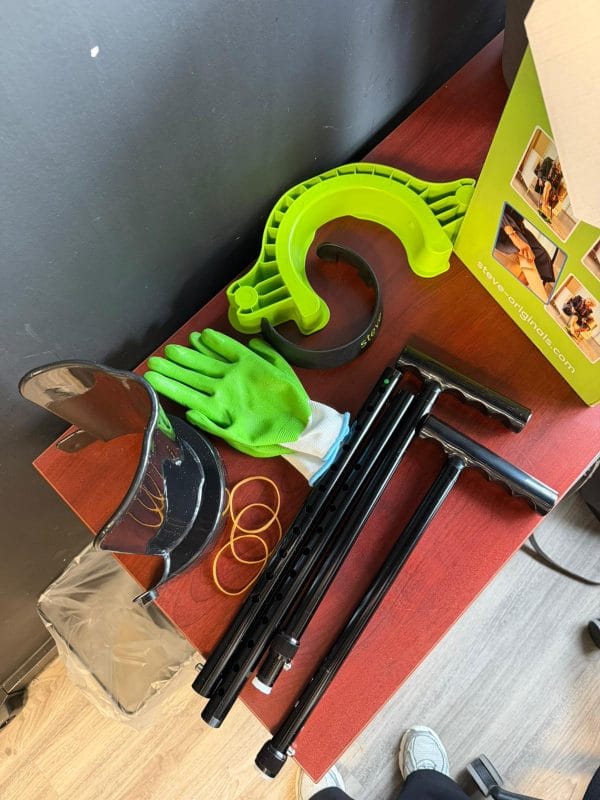 Steve+ aantrekhulp voor steunkousen maat M met groene handschoenen en losse onderdelen op een houten tafel.