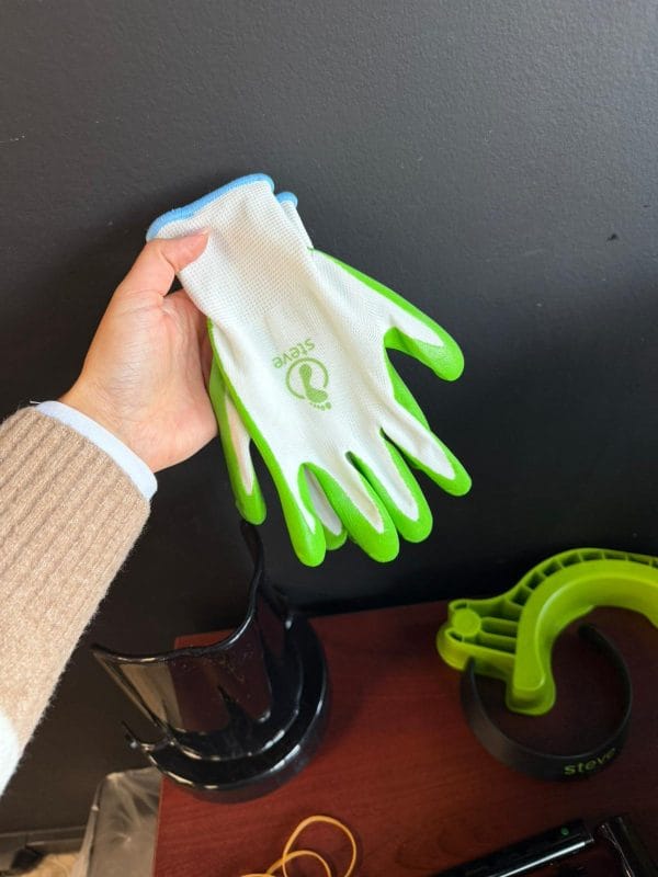 Handschoen voor de Steve+ aantrekhulp voor steunkousen, wit met groene grip en blauw boord, vastgehouden in de hand.