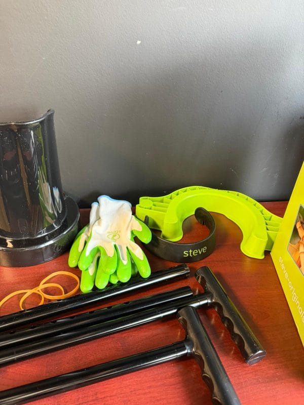 Steve+ aantrekhulp voor steunkousen maat M met groene aantrekbeugel, handschoenen en zwarte handgrepen op tafel.