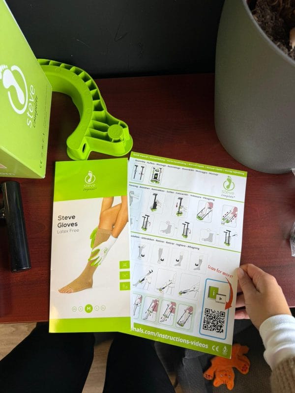 Steve+ aantrekhulp voor steunkousen maat M met groene onderdelen, handleiding en handschoenen op tafel.