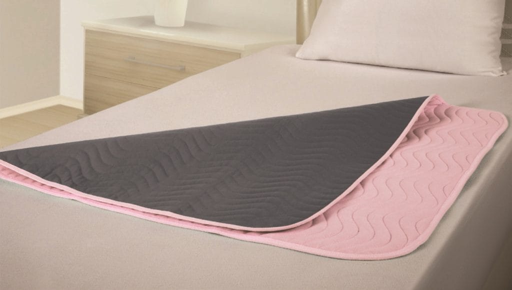 Vida matrasbeschermer met instopstroken in roze en grijs op bed, wasbaar en absorberend tot maximaal 3 liter