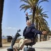 Man rijdt op de Scootmobiel EON over een boulevard met palmbomen en zee op de achtergrond