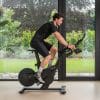 Zwarte Flow Fitness spinningfiets waarop een man binnenshuis traint, voor intensieve fietstraining thuis