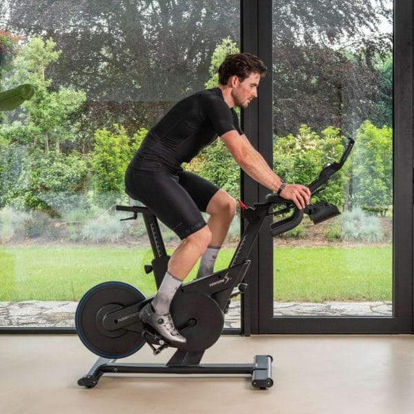 Zwarte Flow Fitness spinningfiets waarop een man binnenshuis traint, voor intensieve fietstraining thuis