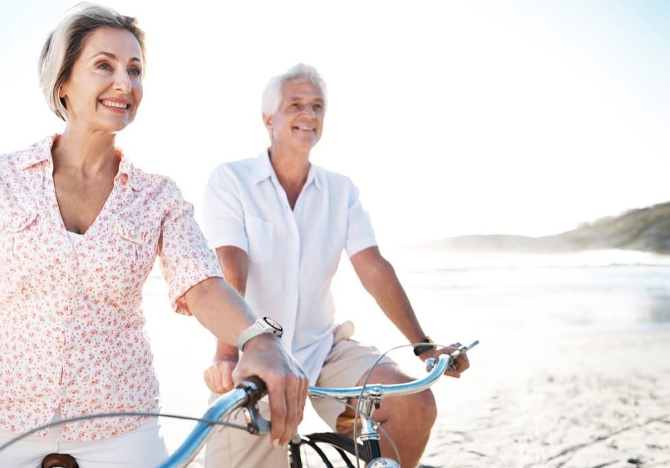 A senior couple riding their bikes together on the beach